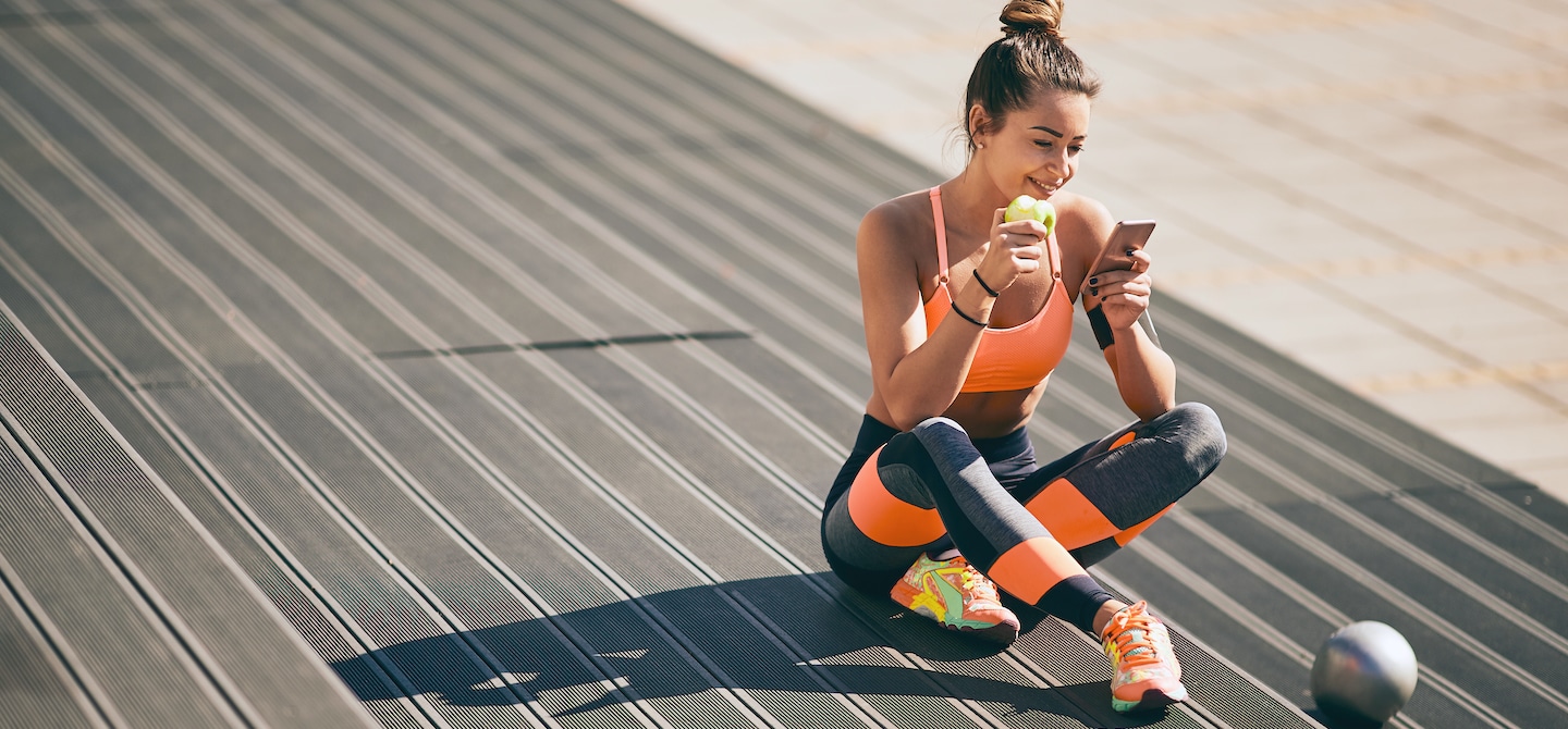 穿着运动休闲装的女人在锻炼前吃着苹果看手机
