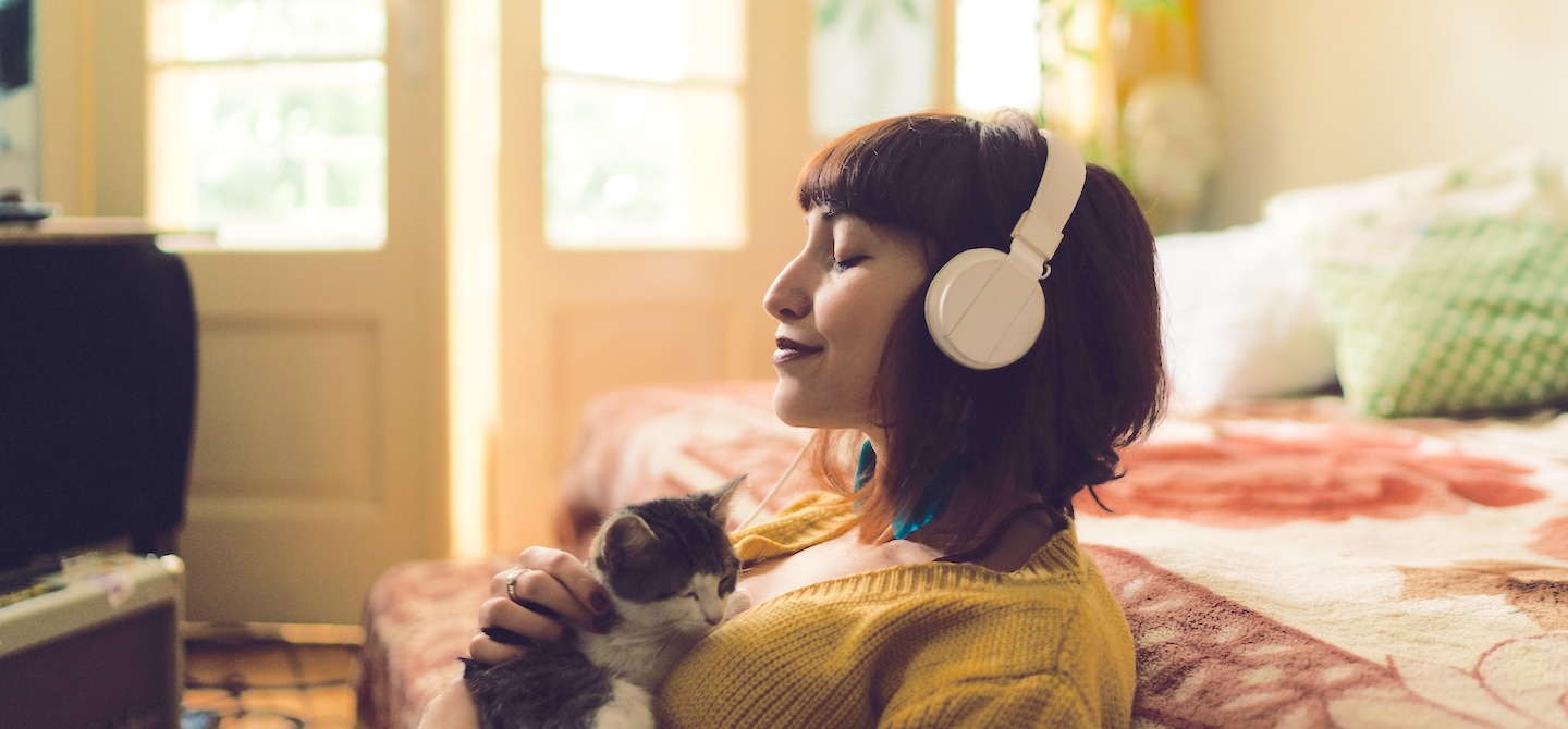 女人在卧室地板上抱着小猫听冥想应用耳机