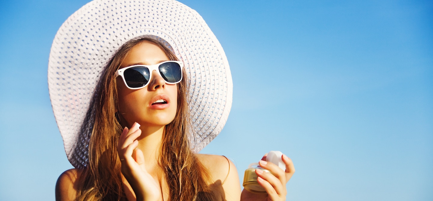 戴着白色遮阳帽和太阳镜的妇女在海滩上涂防晒霜