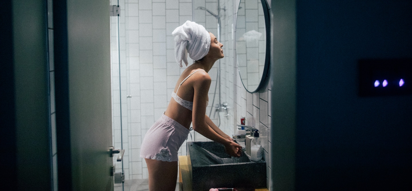 年轻女子用毛巾绕着头在浴室执行她的夜间皮肤例行公事