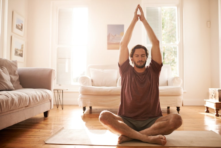一名男子在家中的瑜伽垫上冥想，他把家里变成了一个安静的社交场所