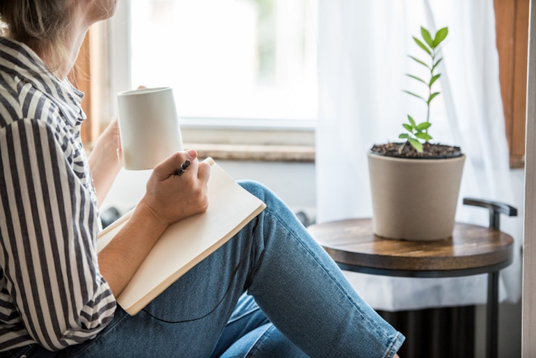 一名女子在窗前端着一杯咖啡写日记，探索如何实现工作与生活的平衡