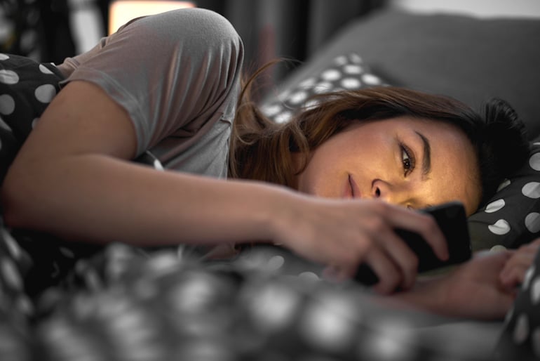 一名女子在床上玩约会软件时使用谢尔比·赛尔斯的虚拟约会技巧