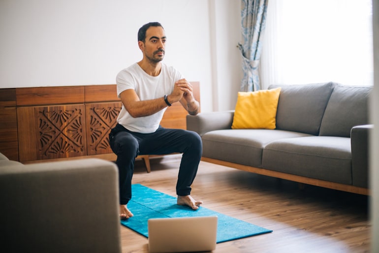 一名男子蹲坐在客厅的蓝色瑜伽垫上