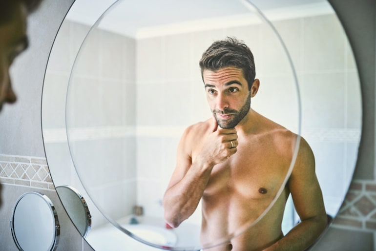 男人在浴室镜子里看着他伟大的皮肤，这要感谢面部精华液的强大功效