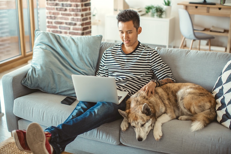 男人在家里用笔记本电脑整理邮件，抚摸着他的狗