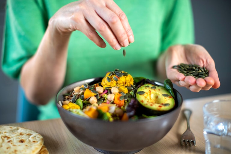 一名女子将南瓜籽扔进她的全麦午餐碗里，说明了健康的生物个体饮食理念
