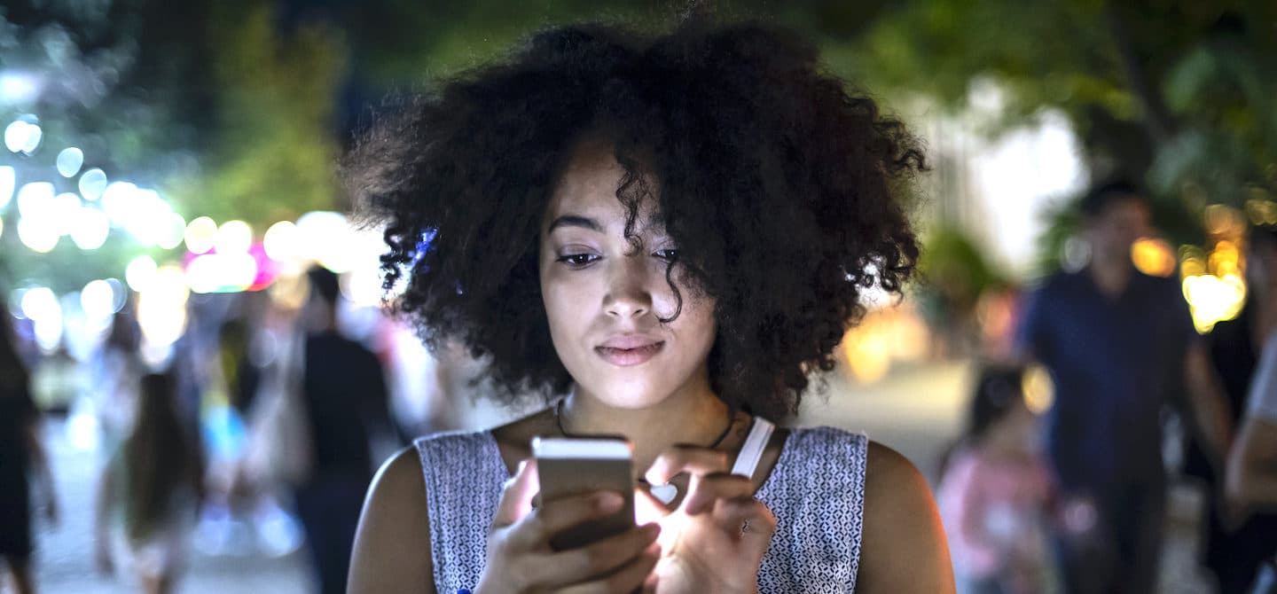 一名妇女在街上使用手机，意识到来自科技产品的蓝光正在伤害她的皮肤