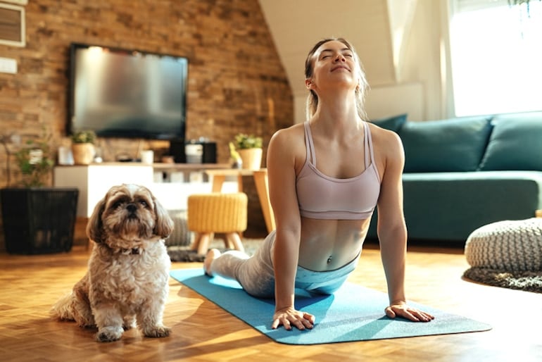 一位女士在家里做瑜伽，旁边她的狗，作为最好的运动之一，缓解压力