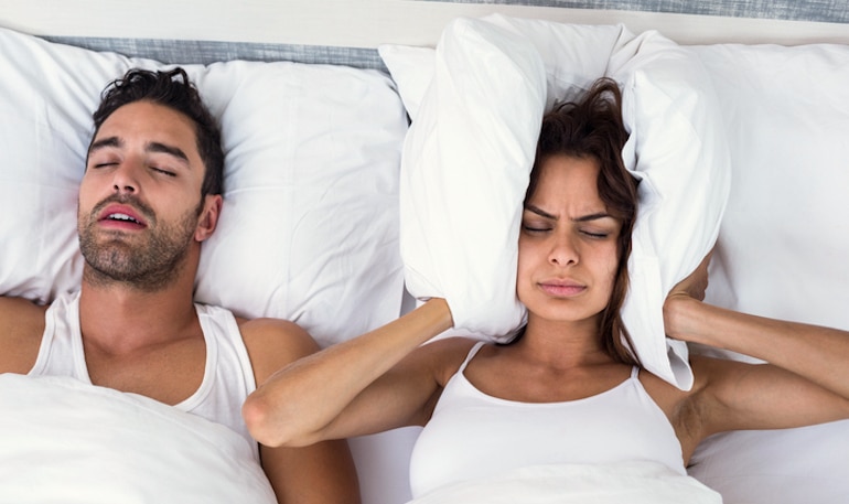 一名女子用枕头堵住了她的耳朵，因为她的男朋友打鼾，睡觉时张大嘴巴
