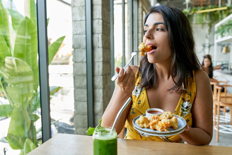 一名妇女在餐厅吃花椰菜，这种食物富含纤维和硫，会导致放屁