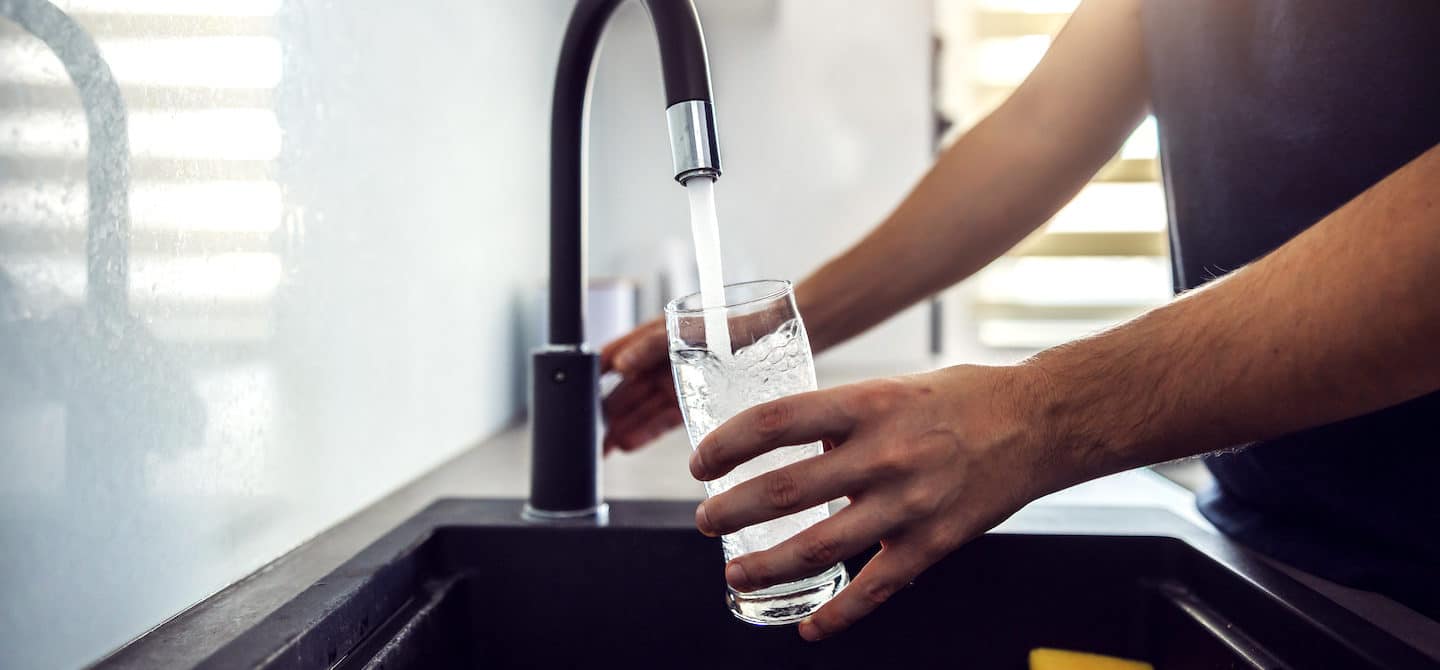 一个男人从厨房水槽里拿一杯水的特写，因为他知道保持水分很重要