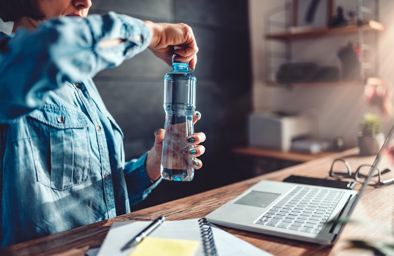 女人在她的办公桌前打开一瓶水，因为补水可以提高你的工作注意力，防止脱水的副作用;这就是为什么保持水分很重要的原因