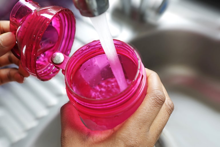 女人的手在水槽的水瓶里装满水，开始她的一天，补水和服用维生素