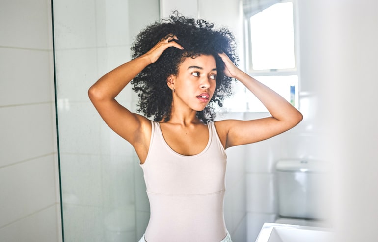 黑人妇女在用发酵米水后对着镜子检查她的头发，看它是否更长、更有光泽