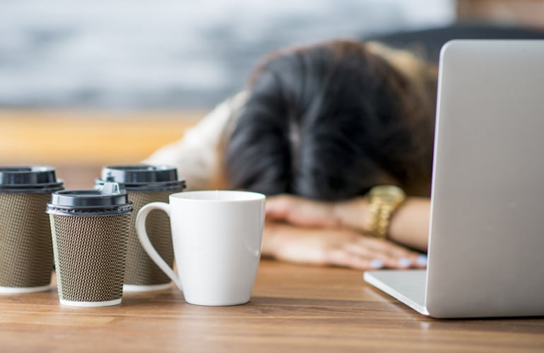 由于咖啡和睡眠不足，疲倦的女人瘫倒在桌子上