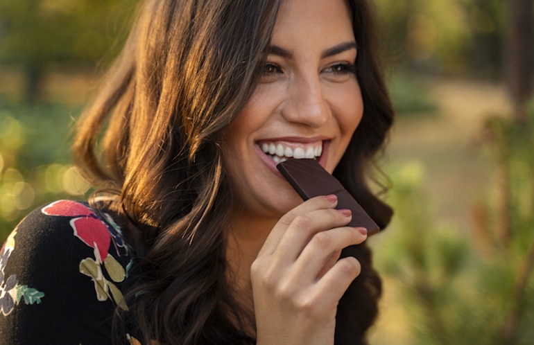 快乐的女人正在吃一块黑巧克力，其中含有镁元素，有助于保护和促进心理健康
