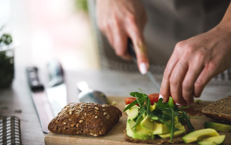 用牛油果、番茄和芝麻菜制作健康素食三明治的人，通过饮食来保持健康