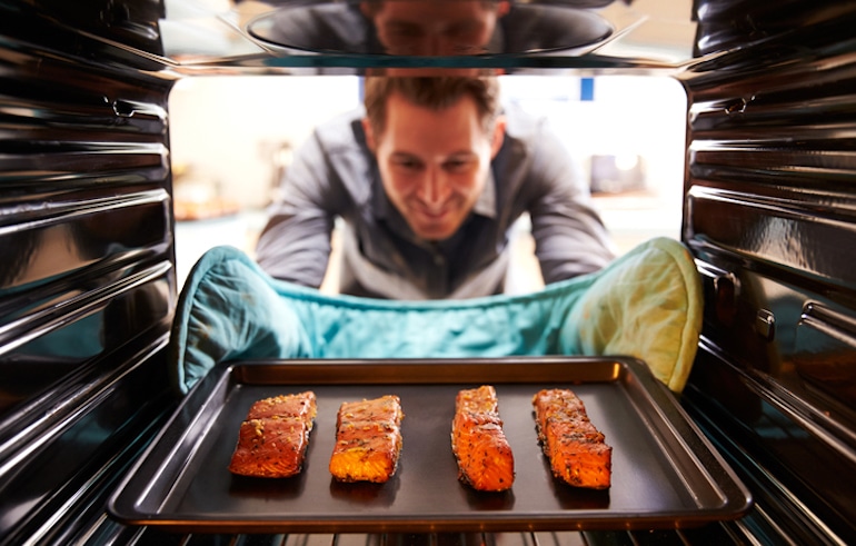 40多岁的男人把三文鱼从烤箱里拿出来，以增加ω -3的摄入量