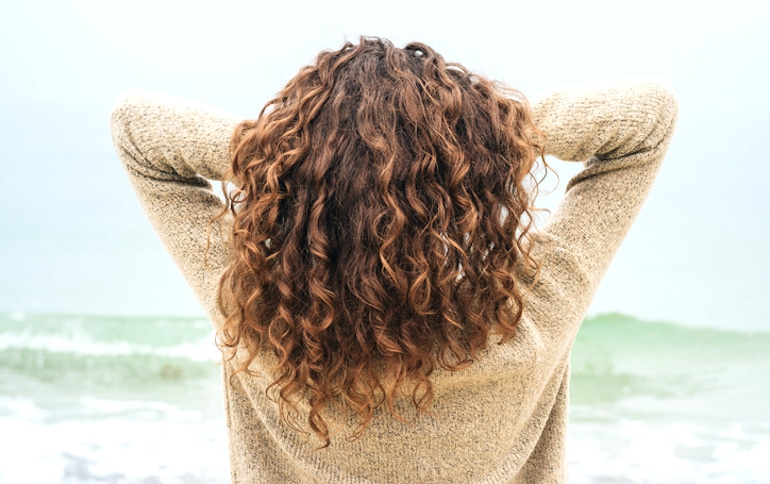 长卷头发的女人在吃完最有利于头发生长的食物后在海滩上弄乱了她的头发