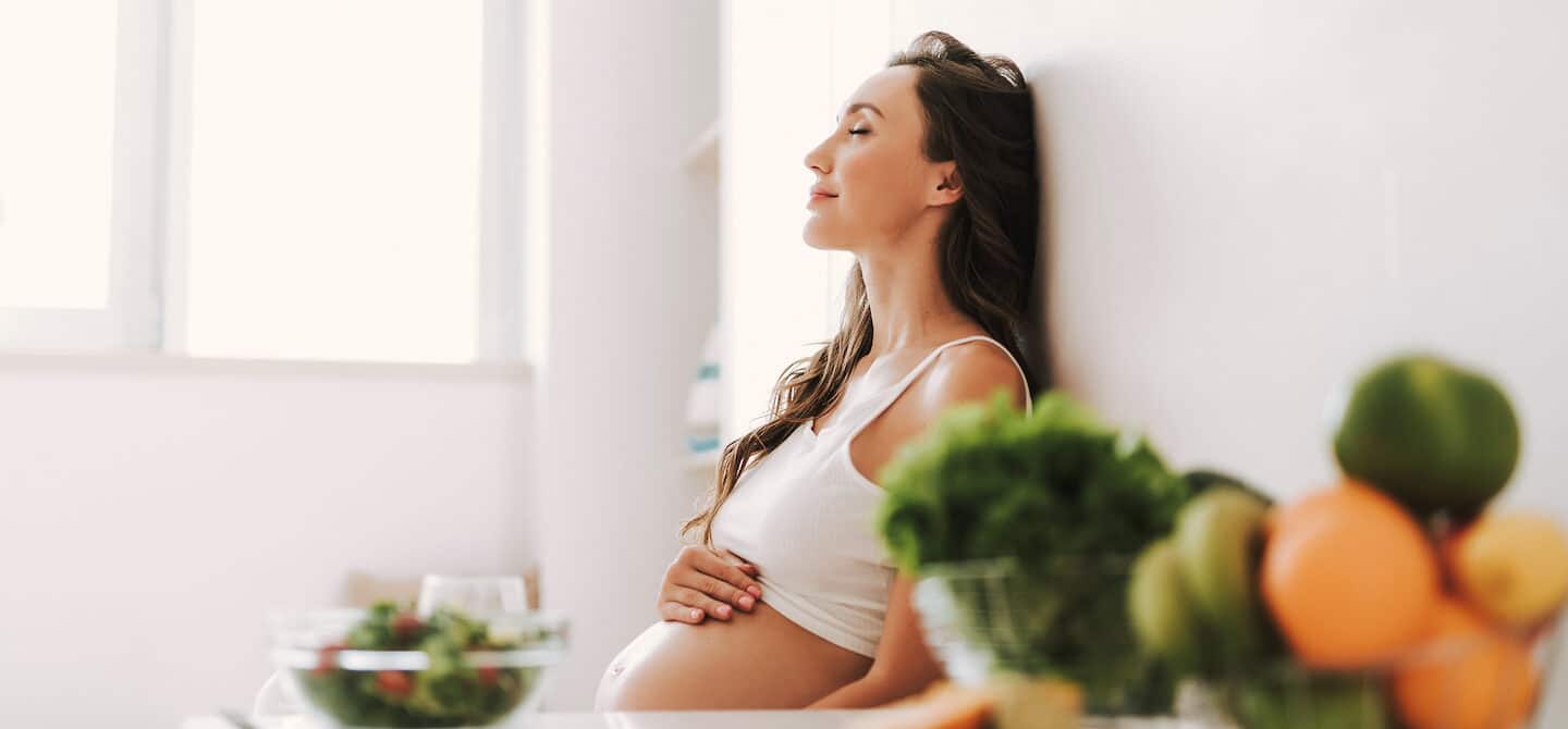 一头长发的孕妇在吃完产前维生素后坐在厨房里